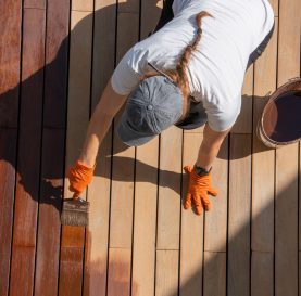 Workwoman staining wood deck boards outdoors, half body overhead view