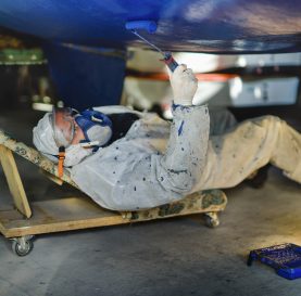 Man painting boat body, maintenance of sailing yacht in boathouse